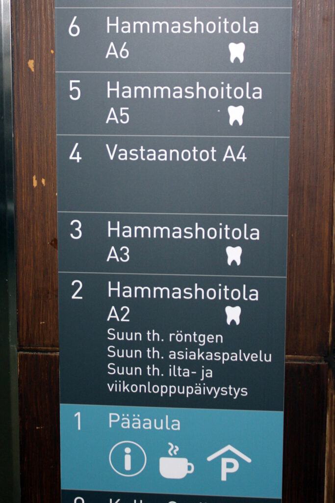 Valokuva hissin luona olevasta opastekyltistä, jossa näkyy rakennuksen kerrokset ja mitä toimintoja kerroksissa on. 