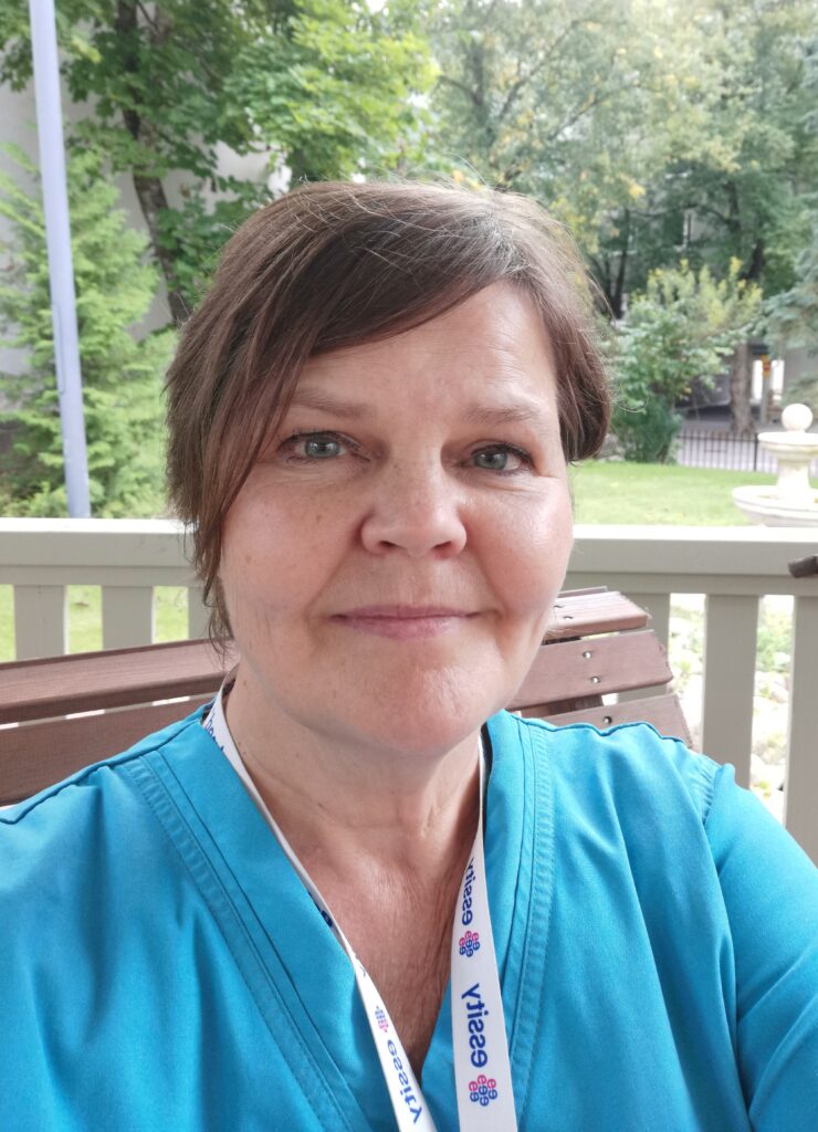 Kuvassa Helena Jauhiainen pukeutuneena siniseen työasuun. Helena katsoo kameraan.