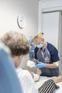 Sairaanhoitaja hoitaa asiakkaan haavaa maski kasvoillaan