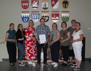 Ryhmäkuva, jossa 8 henkilöä poseeraavat kameralle ruusut ja diplomi kädessään