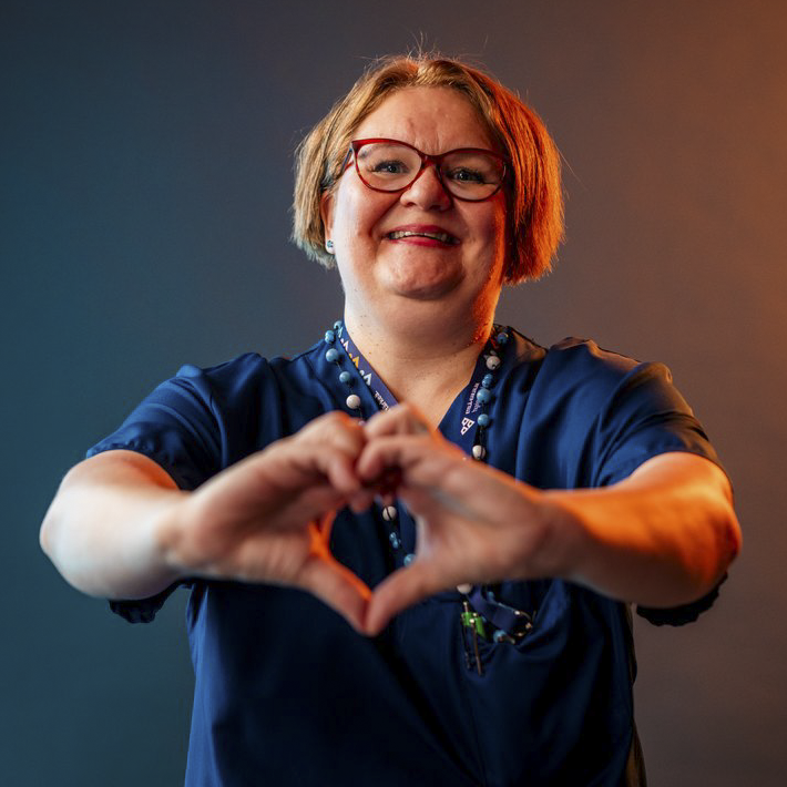 Henkilökuva hoitajasta, joka muodostaa käsistään sydämen.