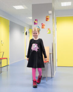 Tyttö kävelee iloisena kohti hymyillen, musta paita ja pinkit housut päällä