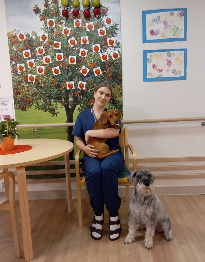 Venla Muuronen Vallikodissa. Venlalla on kuvassa koira sylissään ja toinen istuu hänen vieressään.