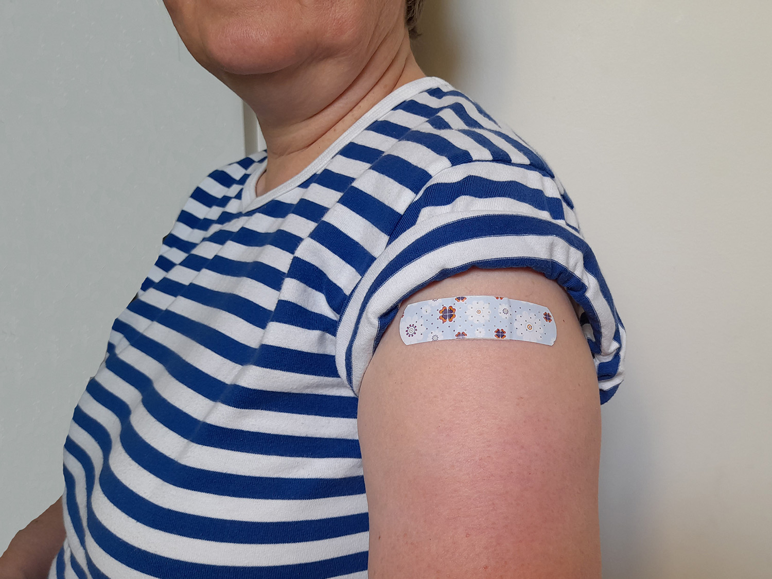 Henkilö lyhythihaisessa sinivalkoraidallisessa paidassa, yläkäsivarressa laastari rokotuksen jälkeen.