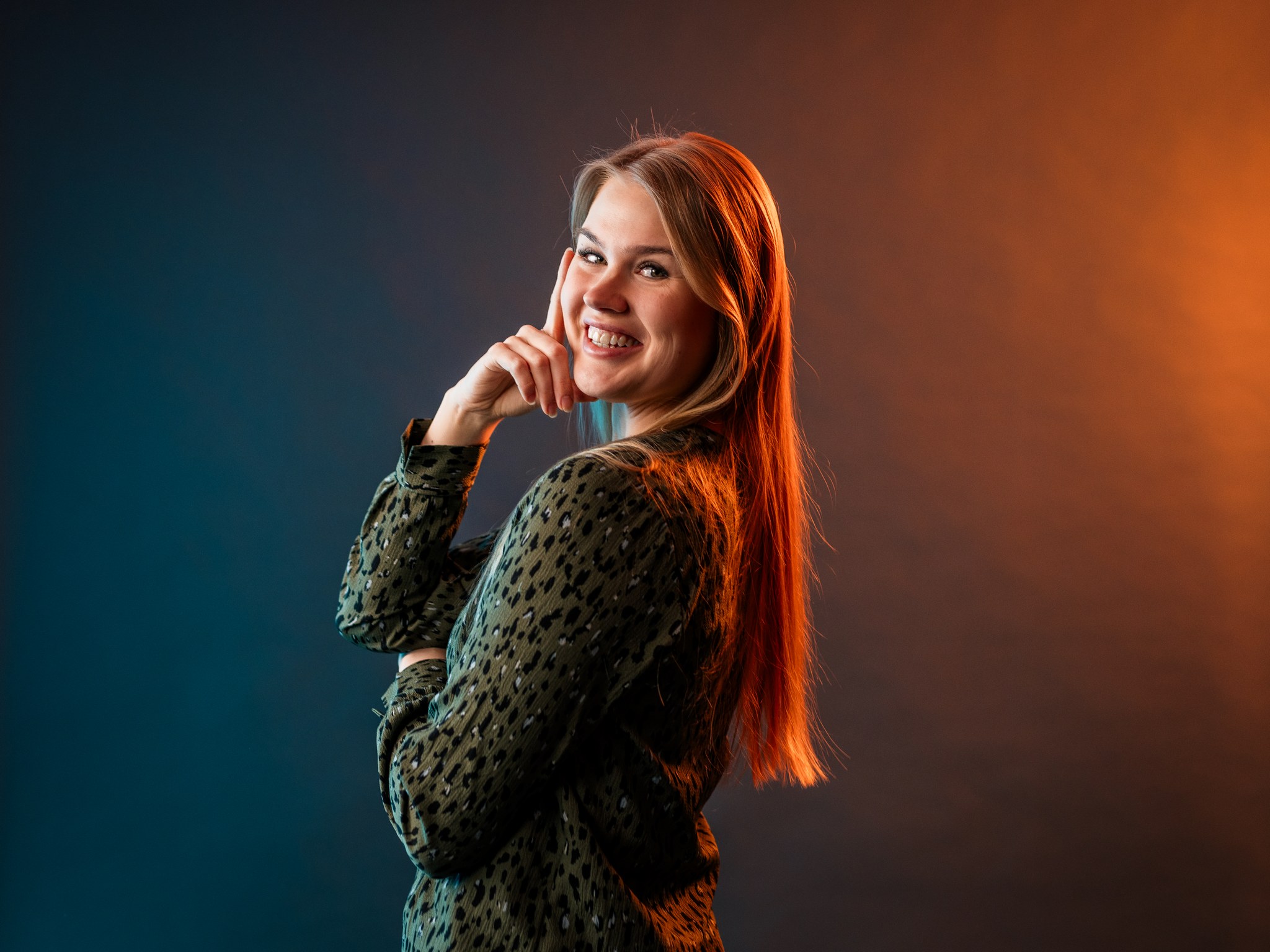 Studiokuva Miiasta, joka seisoo kylki kuvaajaan päin ja nojaa toista kättä kasvoihin etusormi pystyssä.