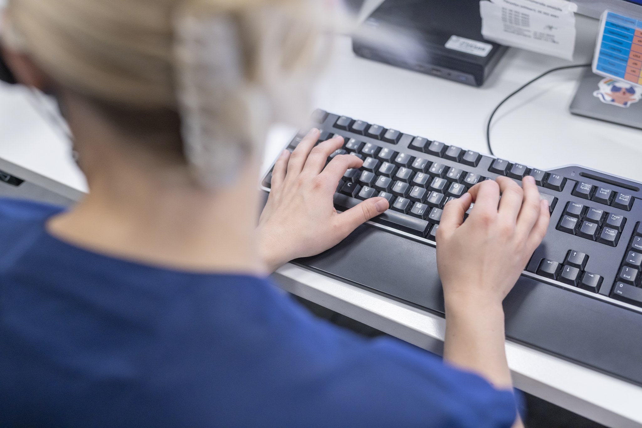 Niskan takaa kuvattu hoitaja, joka kädet näkyvät tietokonenäppäimistöllä.