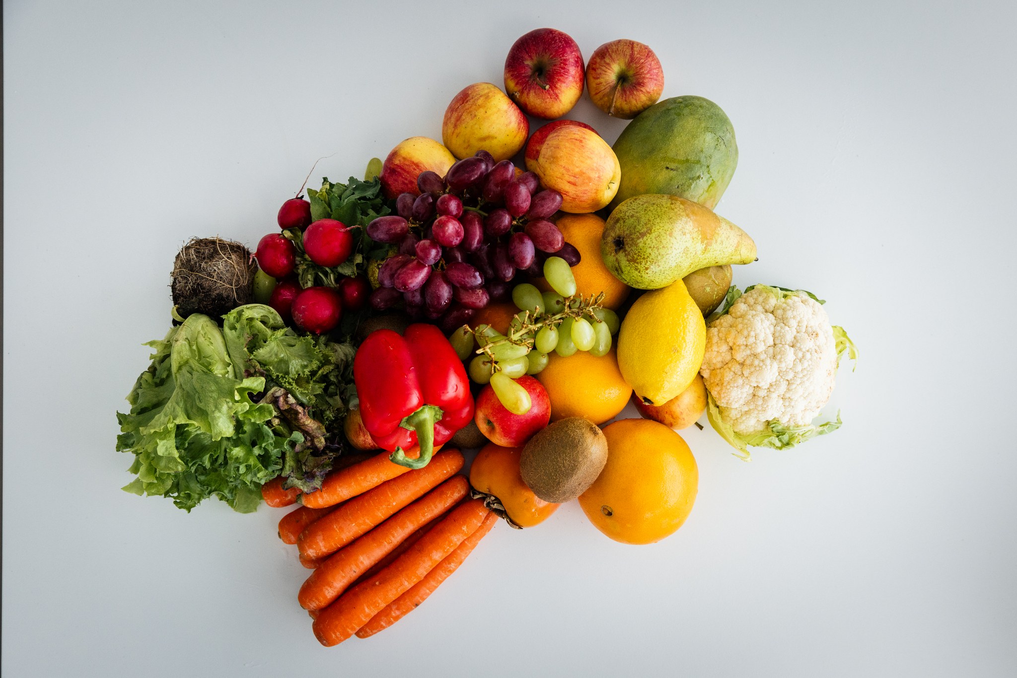 Värikkäitä vihanneksia ja hedelmiä kauniina muodostelmana vaalealla taustalla.