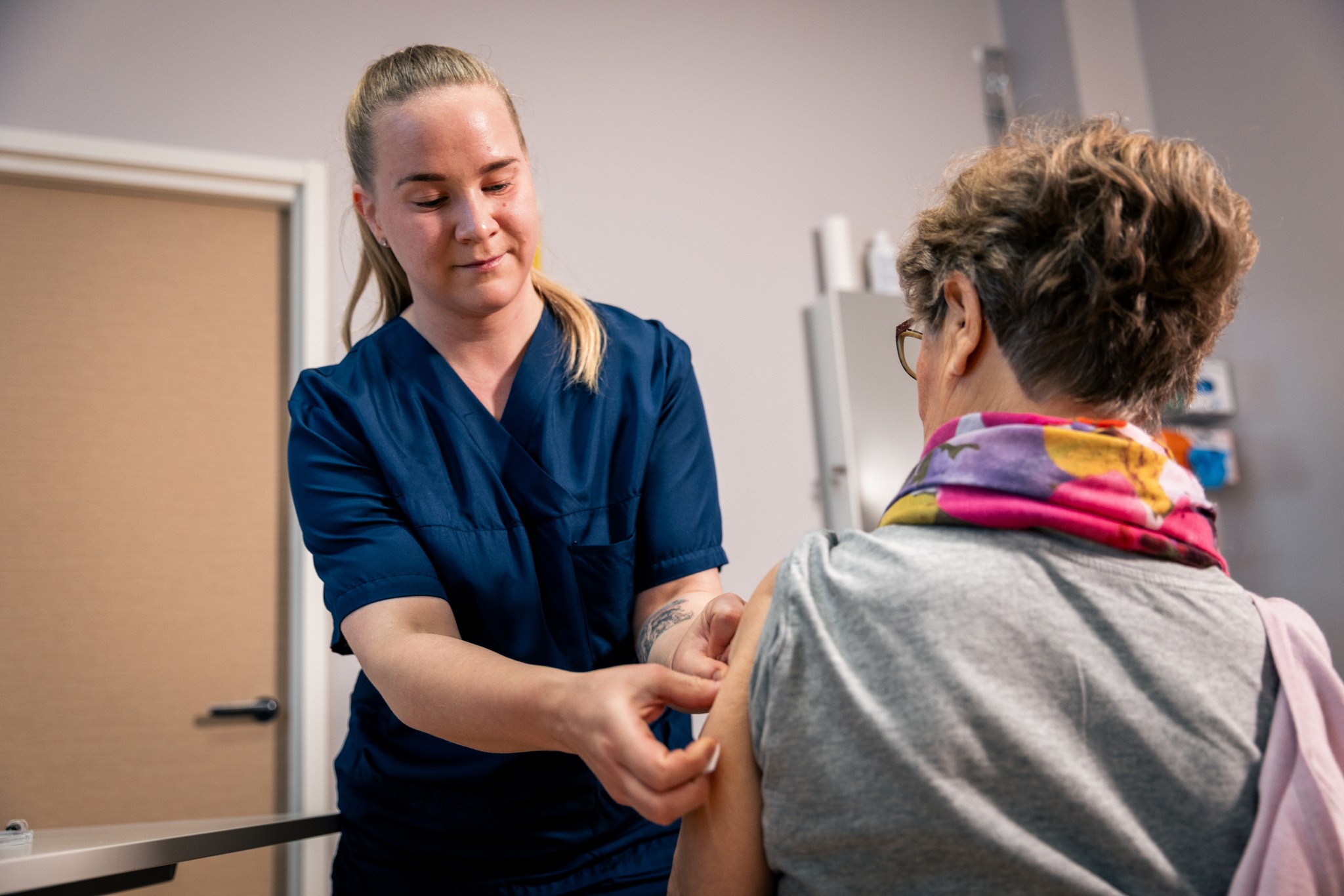 Sairaanhoitaja laittaa laastarin selin kameraan olevan naishenkilön olkapäähän rokotuksen jälkeen.